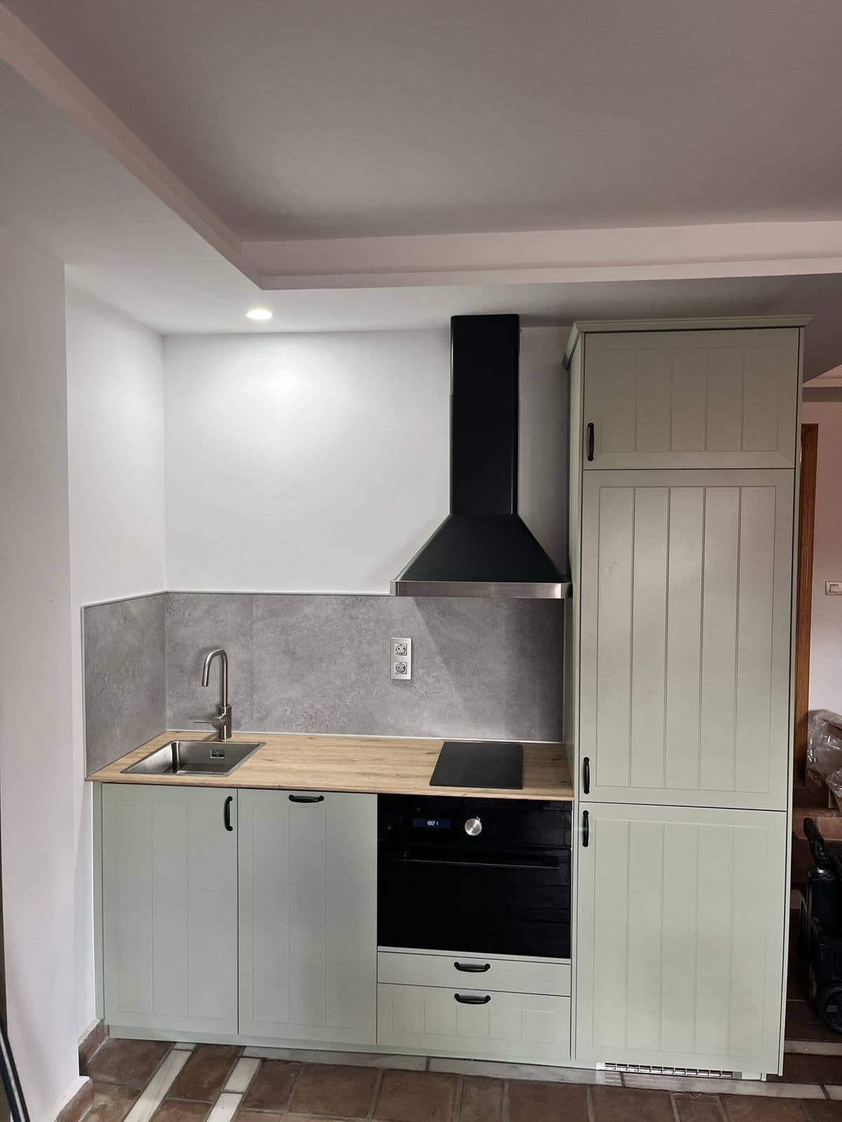 Cocina montada en verde salvia con encimera de madera, horno integrado y campana negra